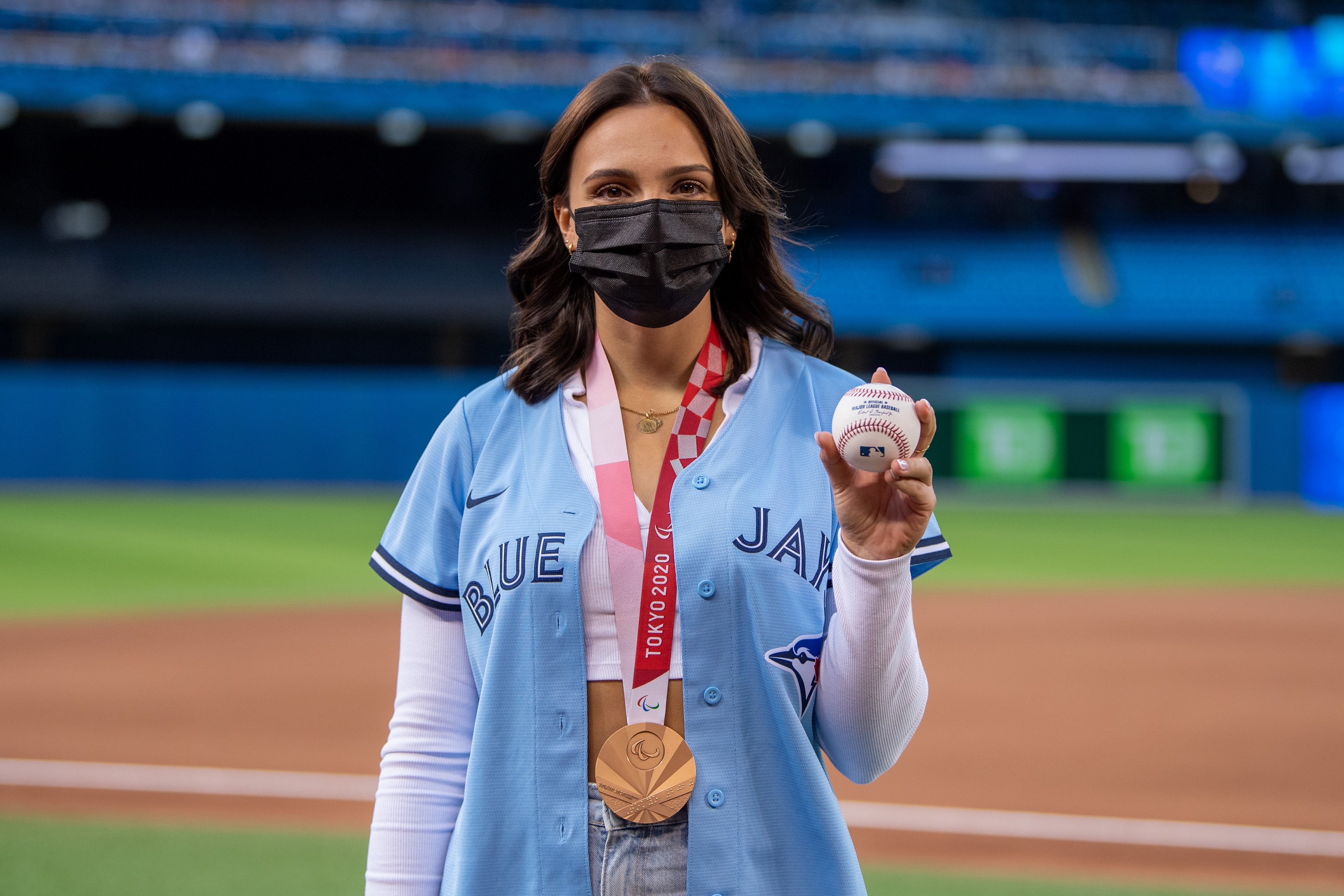 Marissa Papaconstantinou holding a baseball, wearing her bronze medal and a Blue Jays jersey before throwing out the first pitch at the Blue Jays game