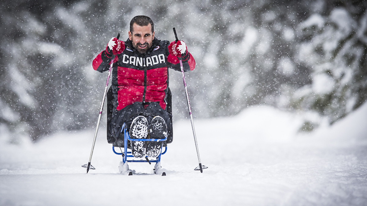 Benoit Huot poles out in a sit ski with the snow falling 