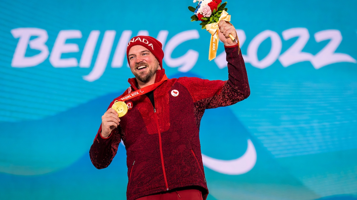 Tyler Turner smiling and holding his gold medal on the podium at the Beijing 2022 Paralympic Winter Games.