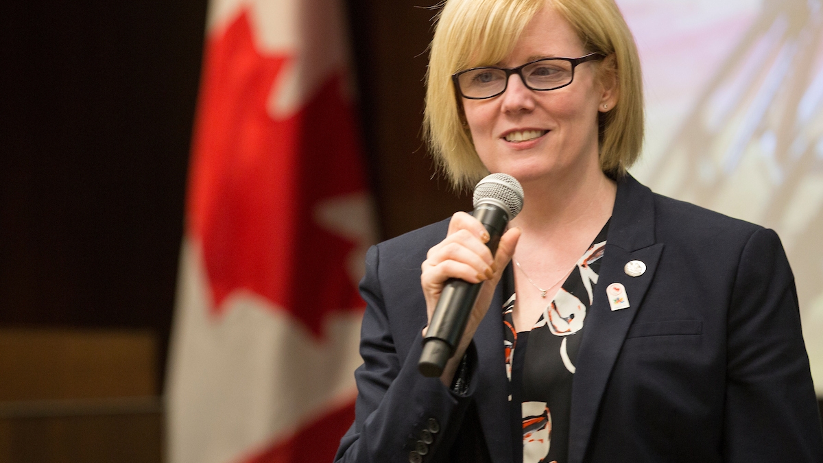 A smiling Carla Qualtrough speaking at an event holding a microphone