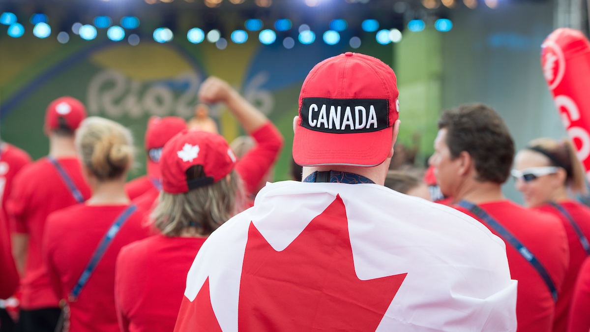 Image of person from behind wearing a Canada hat backwards draped in the Canadian flag at the Rio 2016 flag raising ceremony