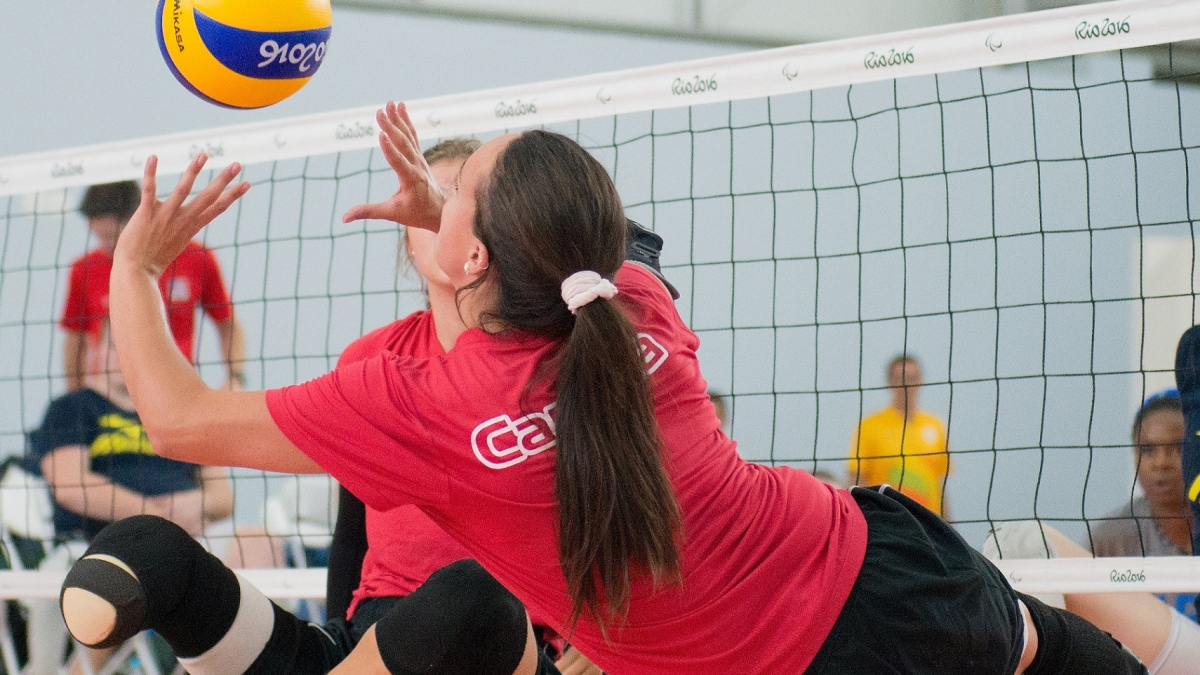 A sitting volleyball player in a Canada shirt hits the ball. 