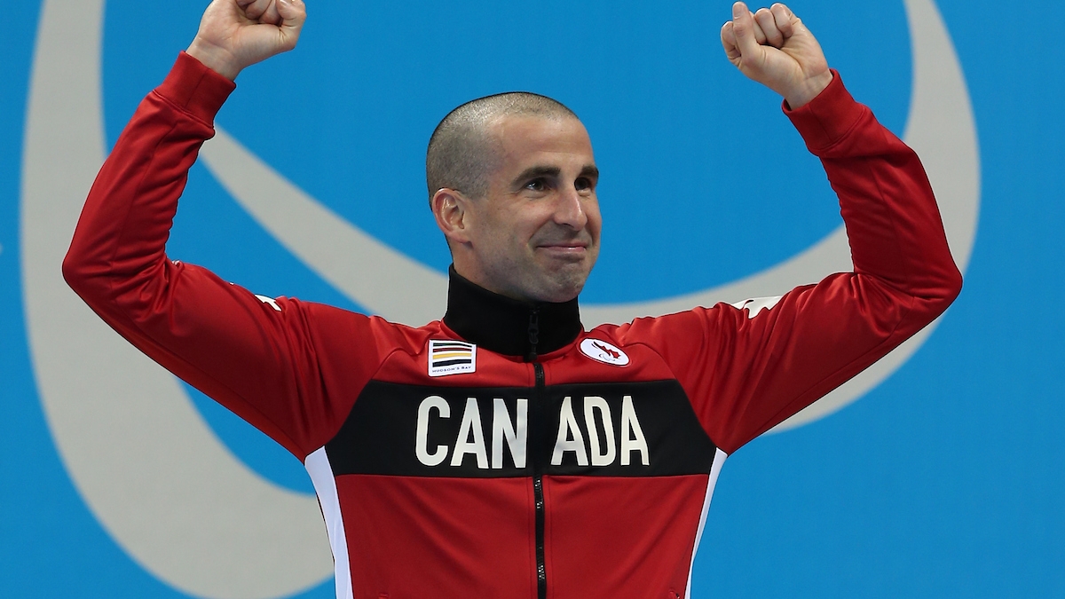 Benoit Huot with his arms in the air celebrating on the podium. 