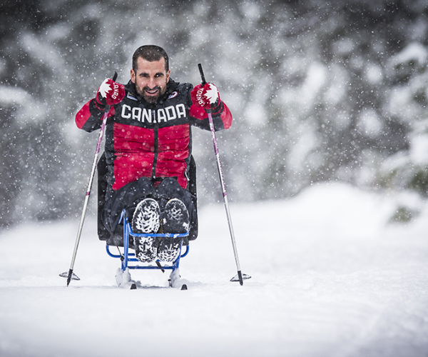 Benoit Huot poles out in a sit ski with the snow falling 
