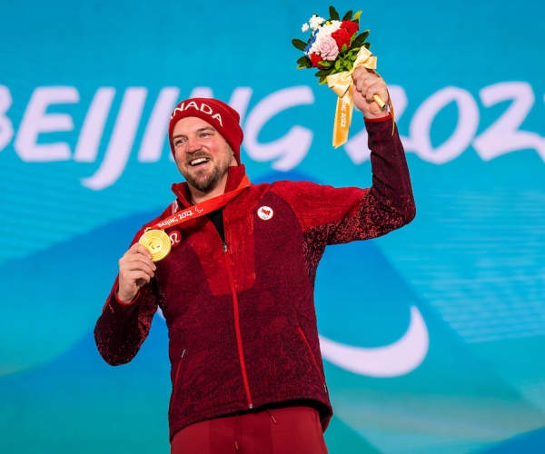 Tyler Turner smiling and holding his gold medal on the podium at the Beijing 2022 Paralympic Winter Games.