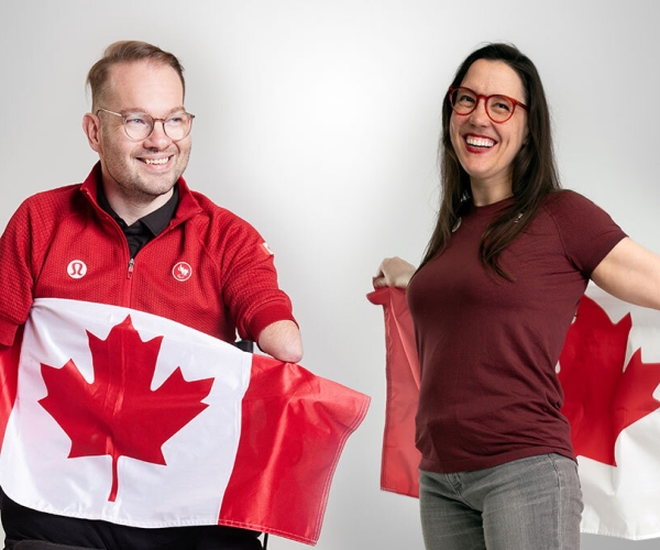 Josh Vander Vies and Karolina Wisniewska, both smiling while wearing red lululemon shirts and holding the Canadian flag