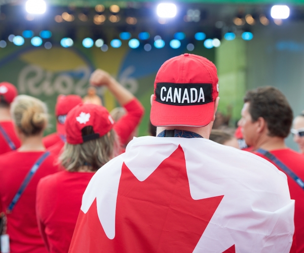 Image of person from behind wearing a Canada hat backwards draped in the Canadian flag at the Rio 2016 flag raising ceremony