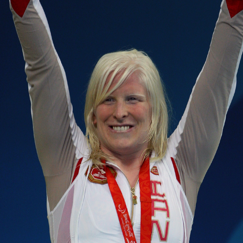 Canadian Paralympian Chelsey Gotell celebrates on the podium with arms raised, wearing her medal and Team Canada tracksuit at the Paralympic Games.