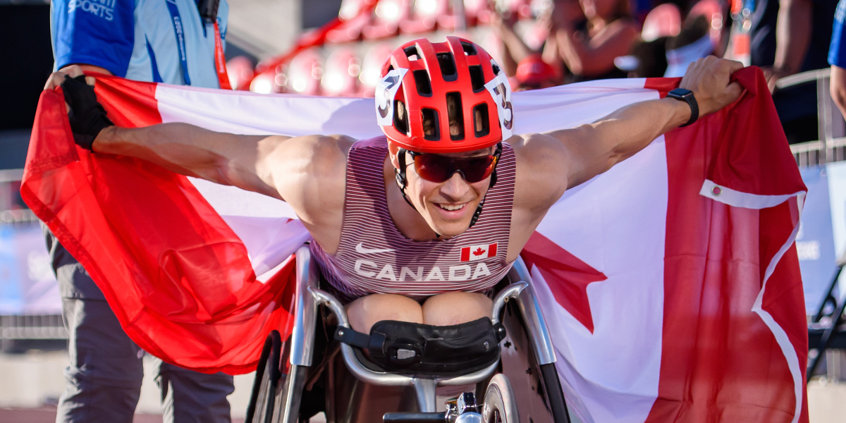 Canadian Wheelchair racer Anthony Bouchard celebrates with holding the Canadian flag behind him with his outstretched arms at the Santiago 2023 Parapan American Games.