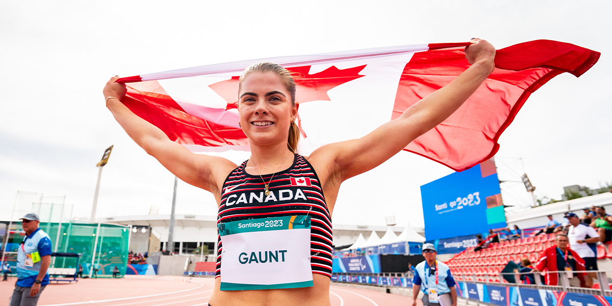 Canadian Para athlete Keegan Gaunt celebrates following a race at the Santiago 2023 Parapan American Games by holding the Canadian flag high between her two outstretched arms.