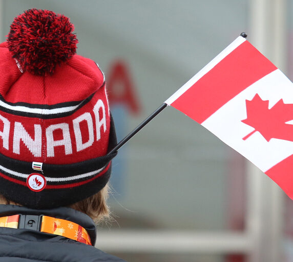 The back of a person's head wearing a Team Canada toque with a Canadian flag sticking out of the hat