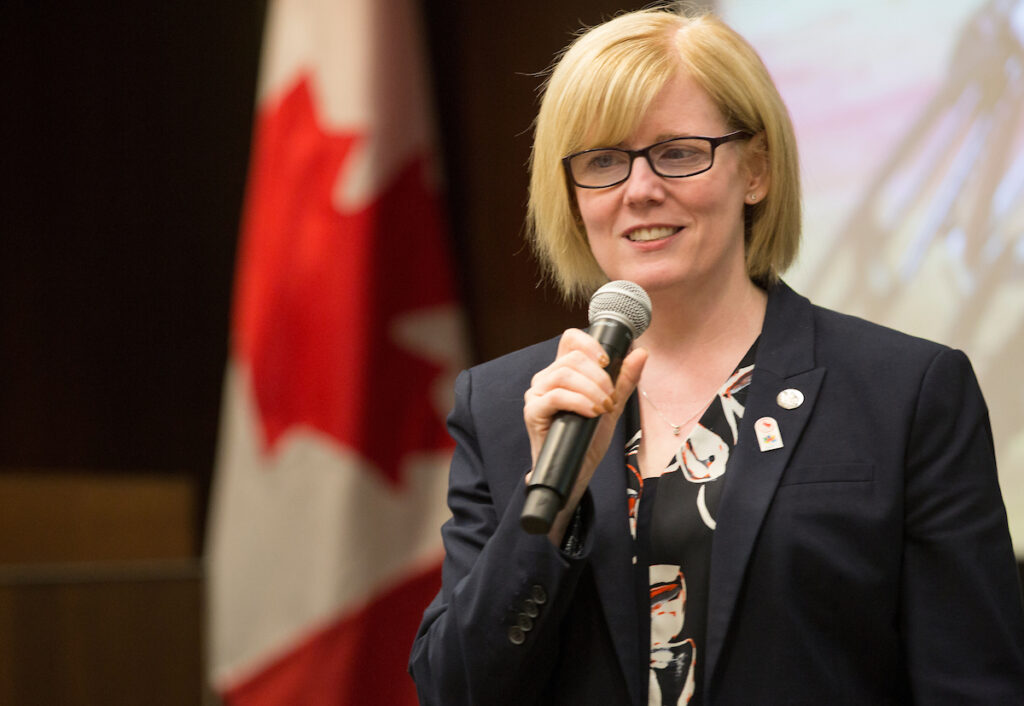 A smiling Carla Qualtrough speaking at an event holding a microphone