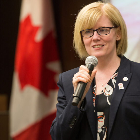 A smiling Carla Qualtrough speaking at an event holding a microphone