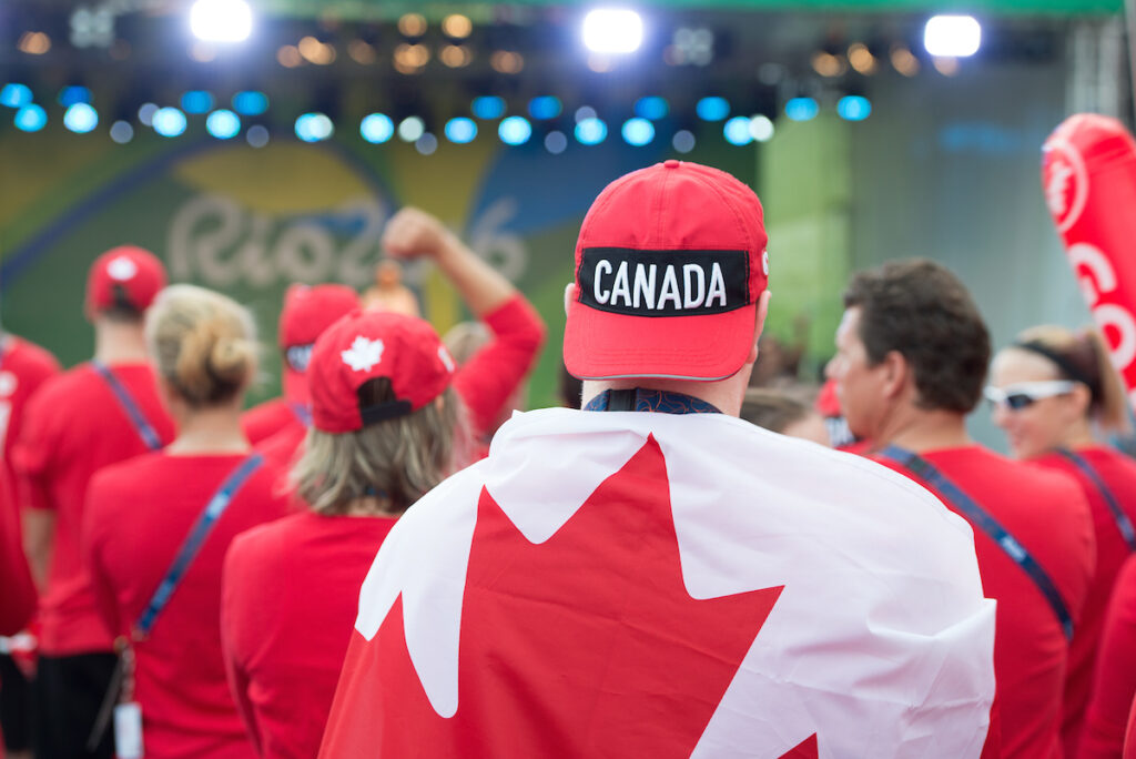 Image of person from behind wearing a Canada hat backwards draped in the Canadian flag at the Rio 2016 flag raising ceremony