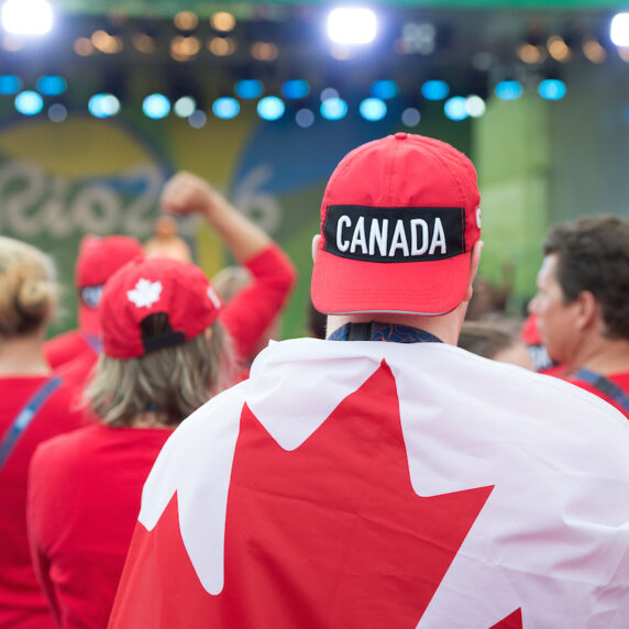 Image of person from behind wearing a Canada hat backwards draped in the Canadian flag at the Rio 2016 flag raising ceremony