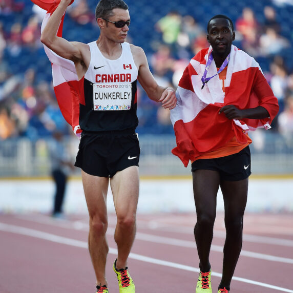 Jason Dunkerley running with his guide in Toronto 2015 carrying the Canadian flag