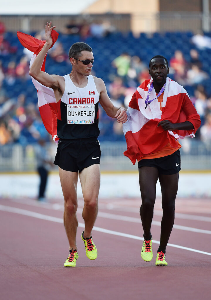Jason Dunkerley running with his guide in Toronto 2015 carrying the Canadian flag