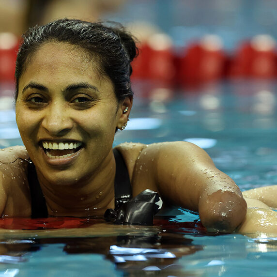 Canadian Para swimmer Katarina Roxon with a joyful expression emerges from the water in an indoor swimming pool, appearing tired but satisfied after a race. | La nageuse canadienne Katarina Roxon, à l'expression joyeuse, sort de l'eau dans une piscine couverte. Elle semble fatiguée mais satisfaite après une course.