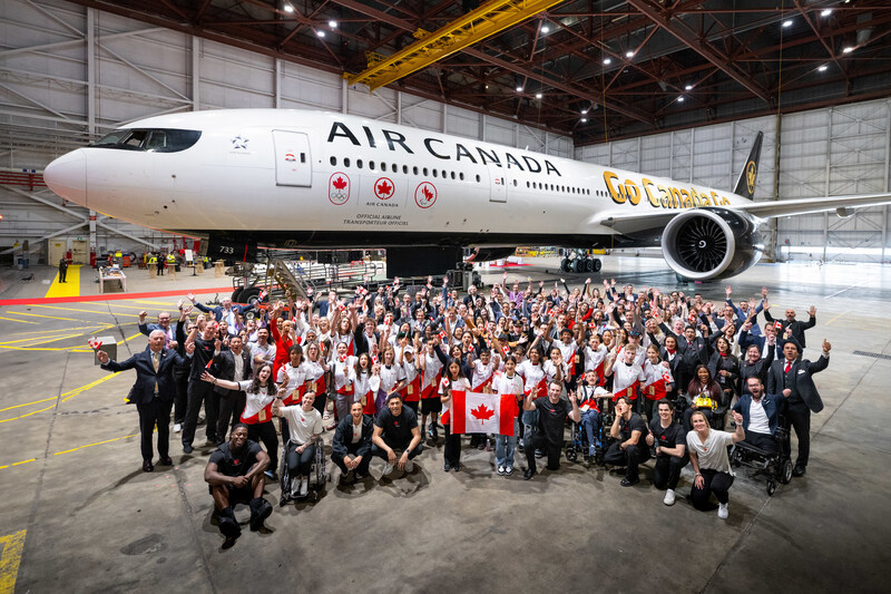 Air Canada plane with the CPC and COC logos on it with a crowd of athletes and supporters standing in front of it in an airport hangar