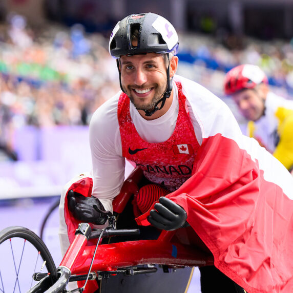 Cody Fournie in his wheelchair after racing, smiling with a Canadian flag around him