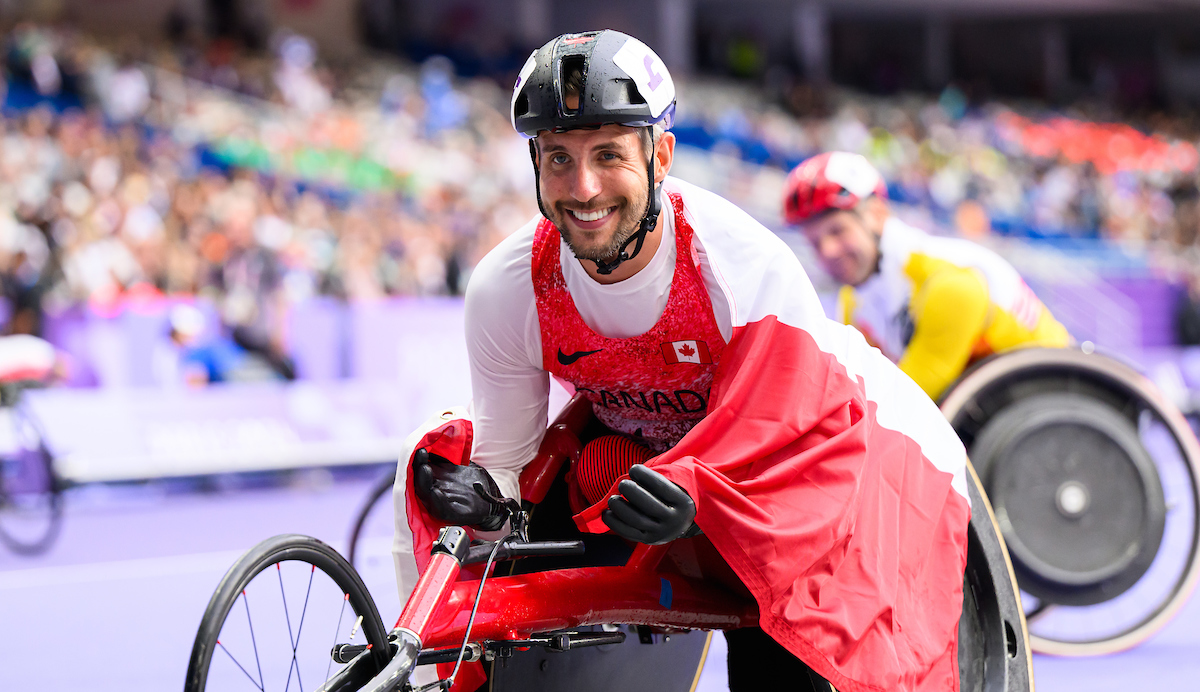 Cody Fournie in his wheelchair after racing, smiling with a Canadian flag around him