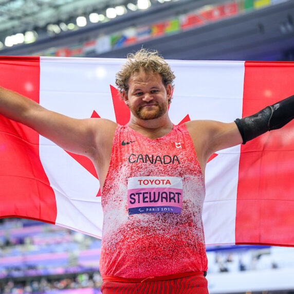 Greg Stewart holds up the Canadian flag after winning a gold medal in shot put