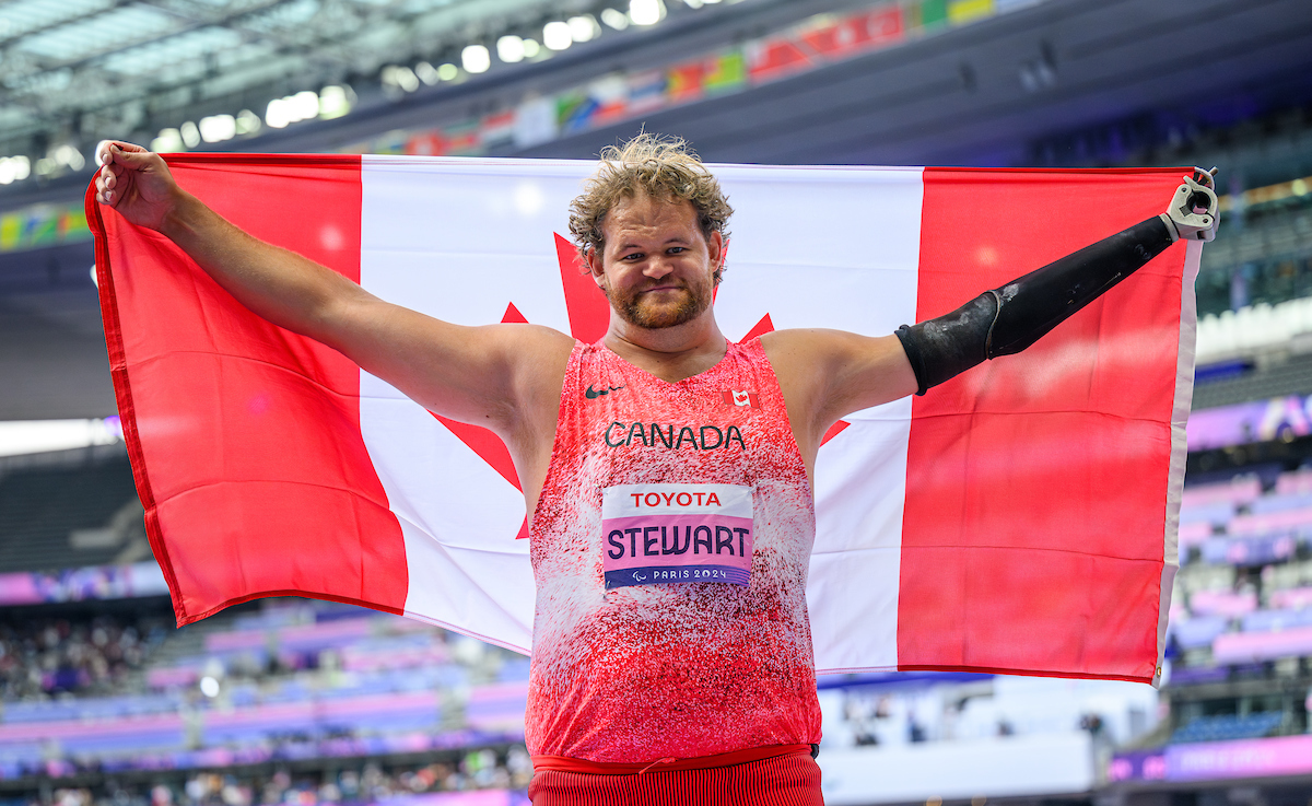 Greg Stewart holds up the Canadian flag after winning a gold medal in shot put