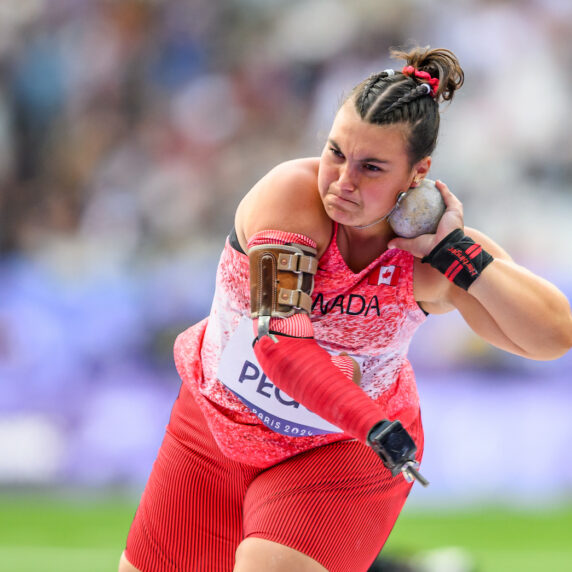 Katie Pegg with the shot put held to her ear mid-throw