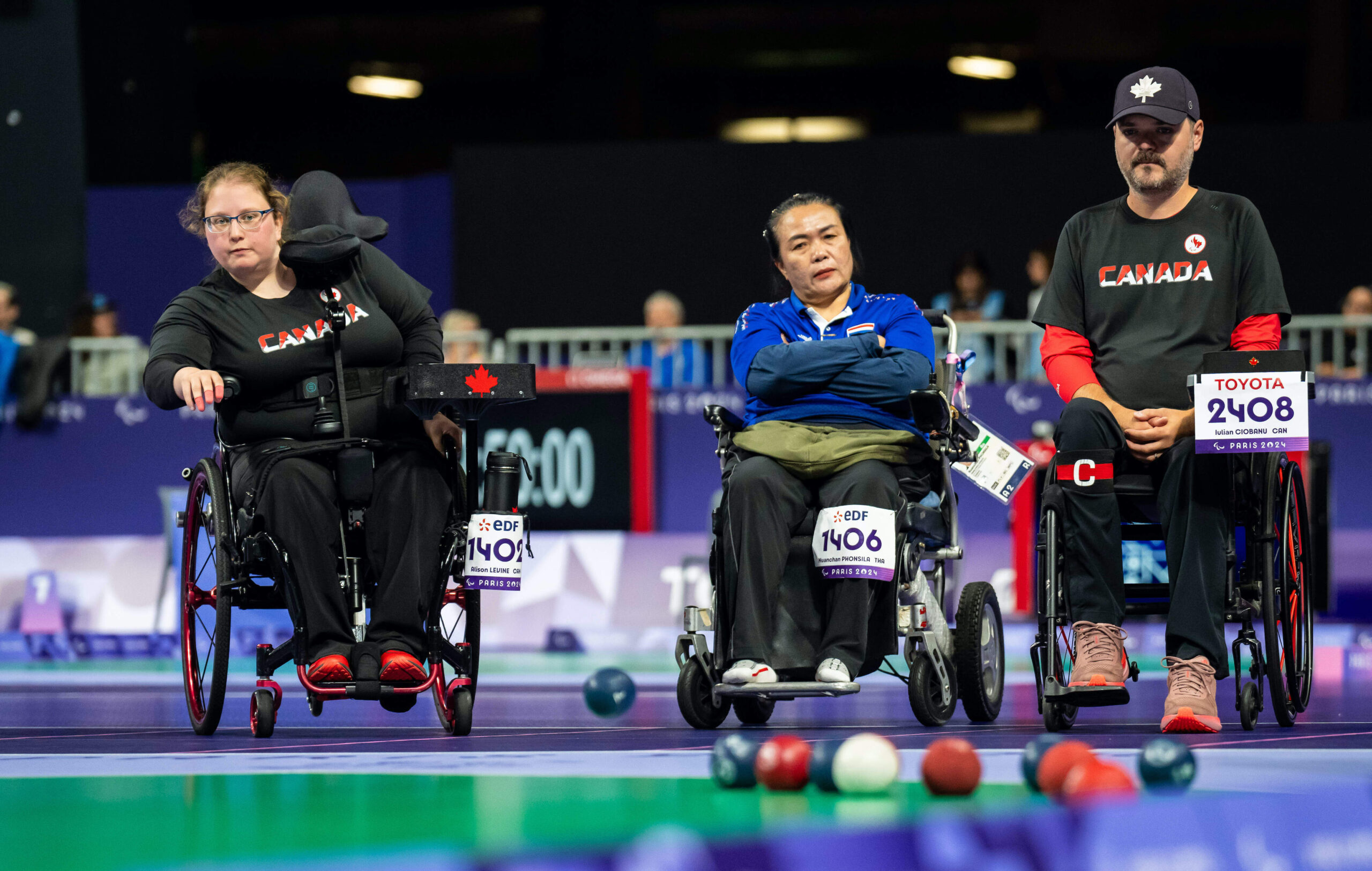 Alison Levine throws a blue ball while Iulian Ciobanu and an opponent watch in front of a set of balls during a match of Boccia.