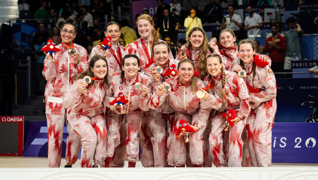 The Canadian women's sitting volleyball team poses, smiling, in their red Lululemon gear with their bronze medals