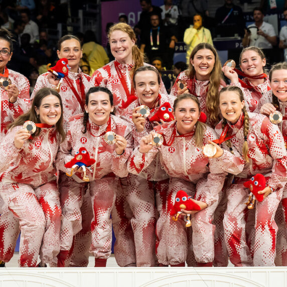 The Canadian women's sitting volleyball team poses, smiling, in their red Lululemon gear with their bronze medals