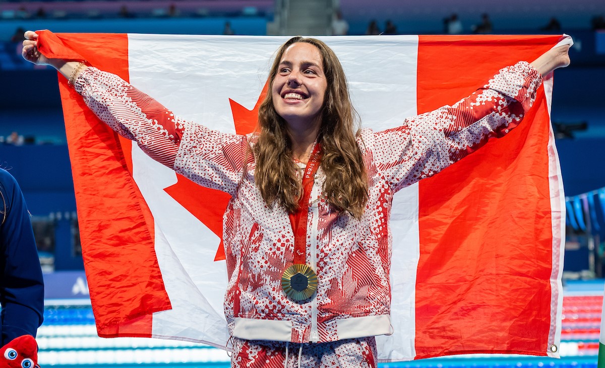 Para swimmer stands on podium holding canada flag behind her back