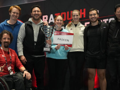 Team members from Fasken, winners of the Vancouver ParaTough Cup, stand together smiling and holding their trophy. Paralympian Josh Dueck is seated in front in a wheelchair, wearing a red shirt. The group poses in front of a ParaTough backdrop.