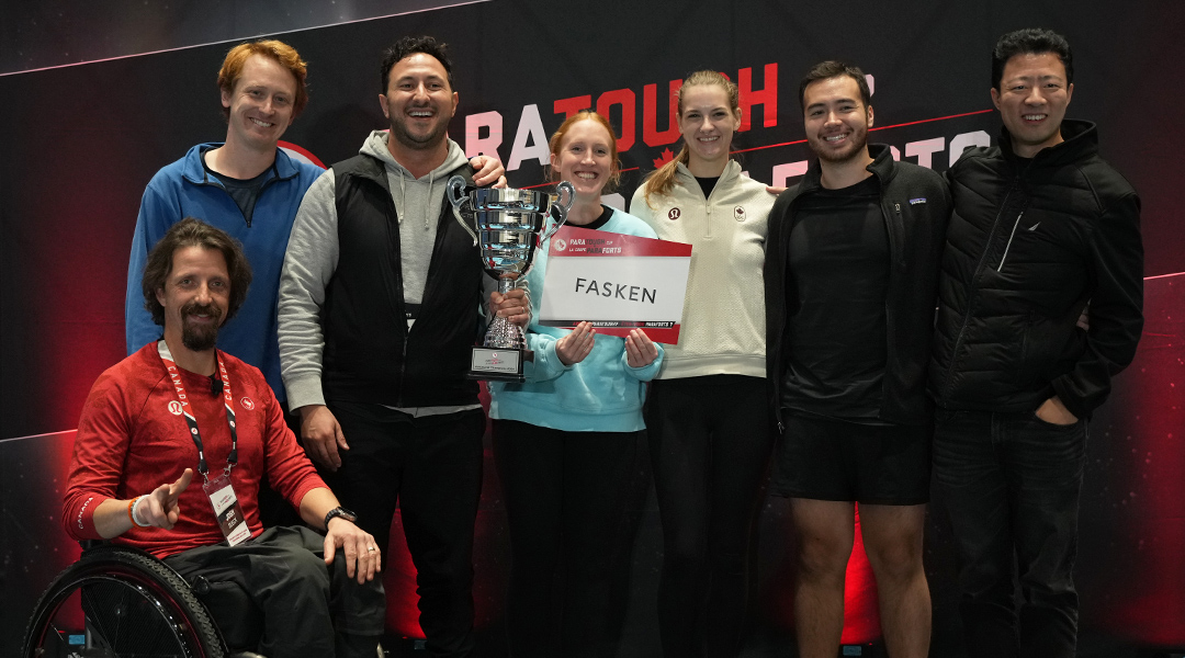 Team members from Fasken, winners of the Vancouver ParaTough Cup, stand together smiling and holding their trophy. Paralympian Josh Dueck is seated in front in a wheelchair, wearing a red shirt. The group poses in front of a ParaTough backdrop.