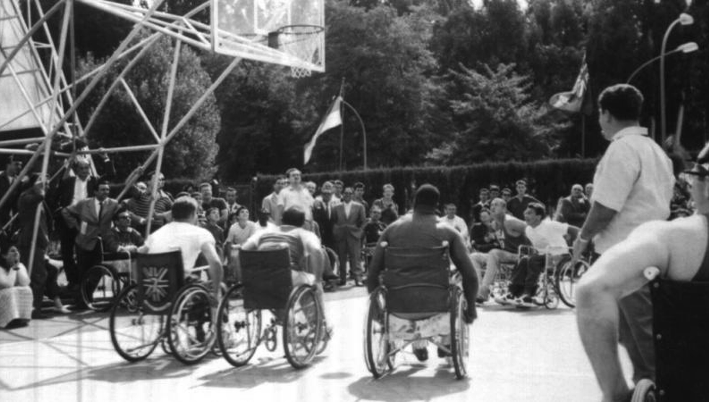 Historic black-and-white image of wheelchair basketball players competing in front of a crowd at the Rome 1960 Paralympic Games, the first official Paralympic Games.