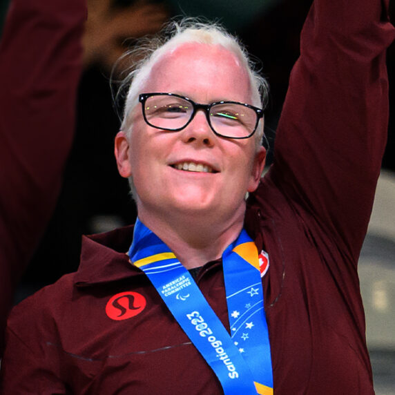 Canadian Goalball player Whitney Bogart celebrates on the podium at the Santiago 2023 Parapan American Games after receiving her gold medal alongside her teammates.