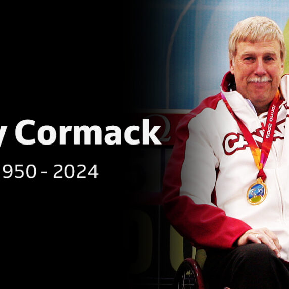 Portrait of Canadian Paralympian Gary Cormack, 1950-2024, wearing a Team Canada jacket and medal, raising his arm in celebration.