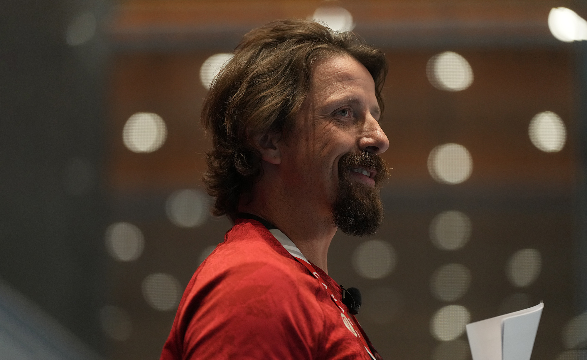 Profile view of Canadian Paralympic gold medallist Josh Dueck smiling, wearing a red shirt and speaking on stage with a microphone headset.