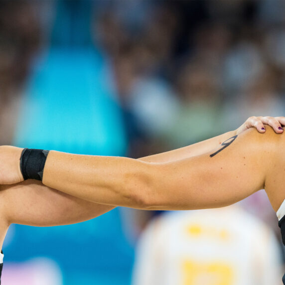 Close-up of two Canadian athletes in black jerseys with red and white lettering, standing shoulder-to-shoulder with arms around each other. The athlete on the right has a braided hairstyle and the number 11 on their jersey.