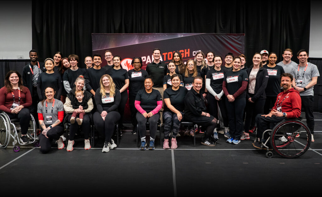 A group photo of Petro-Canada staff and Canadian Paralympians at the ParaTough Cup Calgary event. Participants are gathered in front of a black and red event backdrop with the ParaTough Cup logo, smiling and posing together. Some individuals are seated, including athletes in wheelchairs, while others stand behind them. The group showcases diversity in age, background, and roles, united in support of Para sport.
