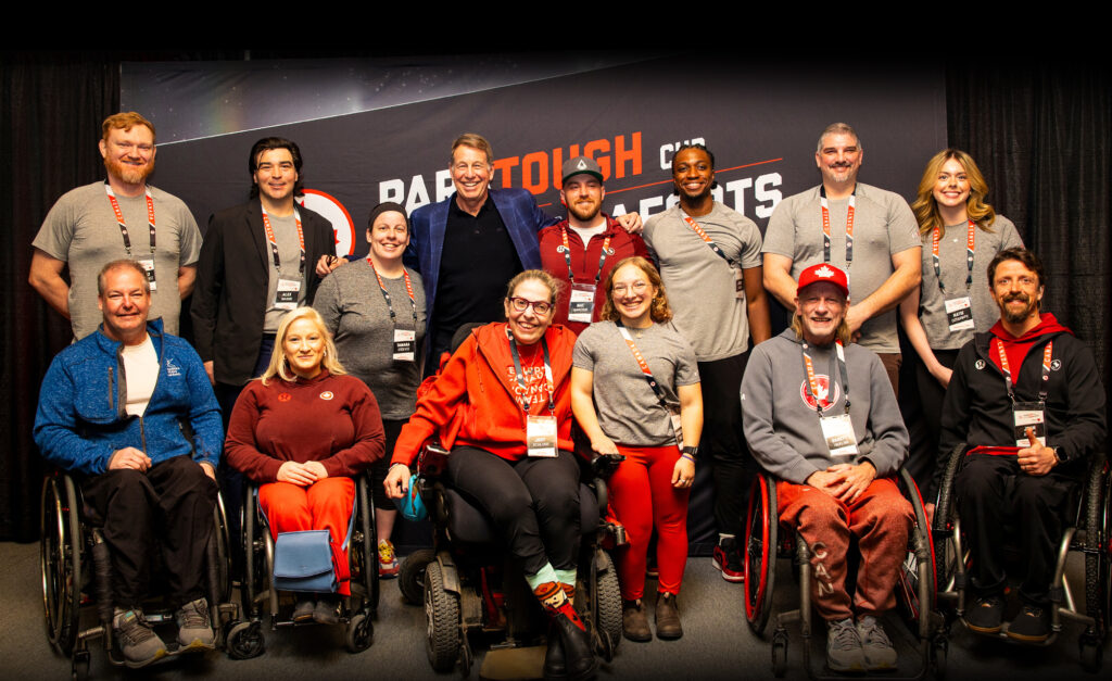 Group photo of Canadian Paralympians, Para sport ambassadors, and CBC broadcaster Scott Russell at the ParaTough Cup fundraising event in Toronto. The group poses smiling in front of a black banner with the event’s logo, celebrating sport and community impact.