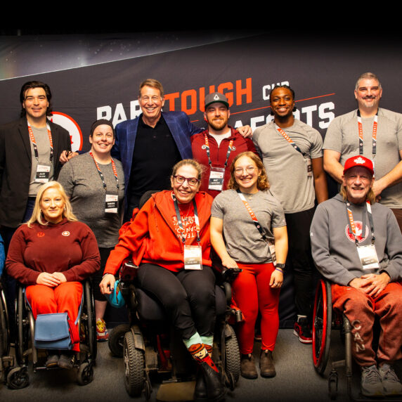 Group photo of Canadian Paralympians, Para sport ambassadors, and CBC broadcaster Scott Russell at the ParaTough Cup fundraising event in Toronto. The group poses smiling in front of a black banner with the event’s logo, celebrating sport and community impact.