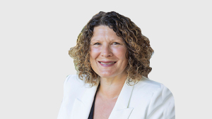 Brenda Plowman, Director at the Canadian Paralympic Committee, smiles while wearing a white blazer and black top against a light grey background.