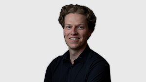 Dane Jensen, Director at the Canadian Paralympic Committee, smiles while wearing a black collared shirt against a light grey background.