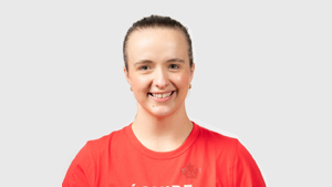 La paralympienne canadienne Heidi Peters sourit en portant un t-shirt rouge d’Équipe Canada, posant devant un fond gris pâle.