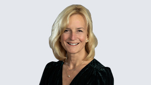 Portrait of Dr. Heather Morrison, smiling, wearing a dark blouse, and standing against a light grey background.