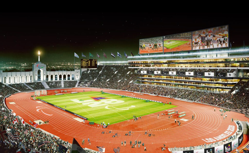 A night-time rendering of the Los Angeles Memorial Coliseum lit up for the LA28 Paralympic Games, featuring a packed stadium with the Paralympic symbol on the field, flags along the top, and large video screens showing Para athletics events.