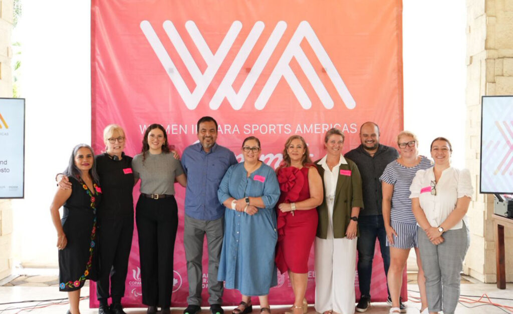 Group photo of speakers and organizers standing in front of a large pink and orange banner that reads “Women in Para Sports Americas” at the 2025 Women in Para Sport Americas Summit.