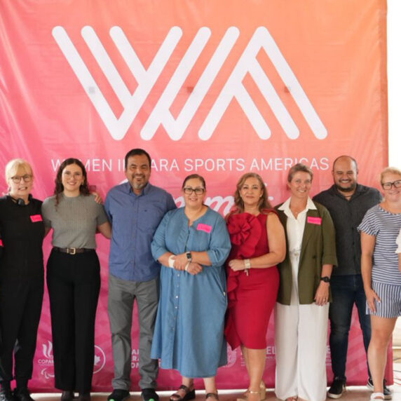 Group photo of speakers and organizers standing in front of a large pink and orange banner that reads “Women in Para Sports Americas” at the 2025 Women in Para Sport Americas Summit.