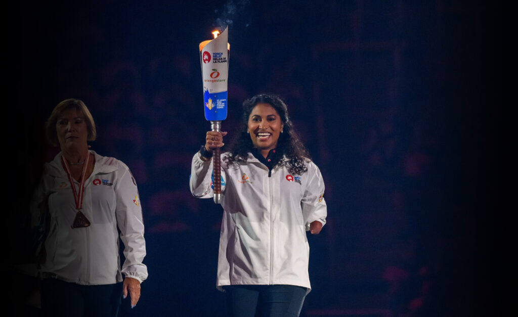 Canadian Paralympian Katarina Roxon smiles while proudly holding the lit torch during the opening ceremony of the 2025 Canada Games. She wears a white Team Newfoundland and Labrador jacket.